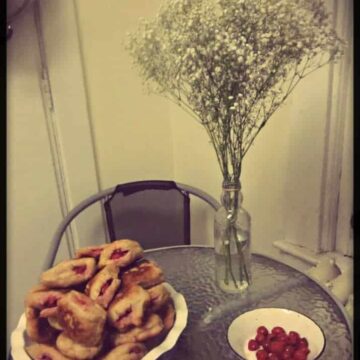 A plate of sour cherry sufganiyot on a table next to a vase of flowers.