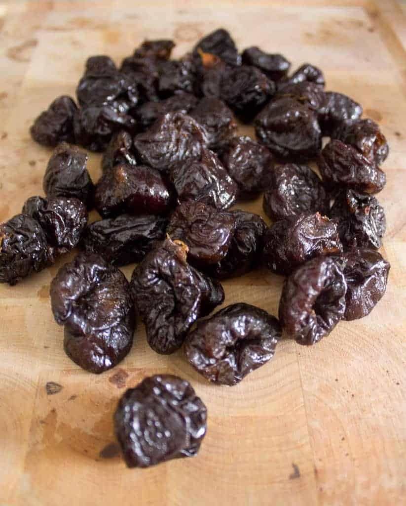 the stars of the show A pile of dried prunes sits artfully spread on a light wooden surface, their dark, glossy skin wrinkled yet inviting. Perfect for crafting delicious prune vegan hamantaschen or simply savoring as a sweet treat.