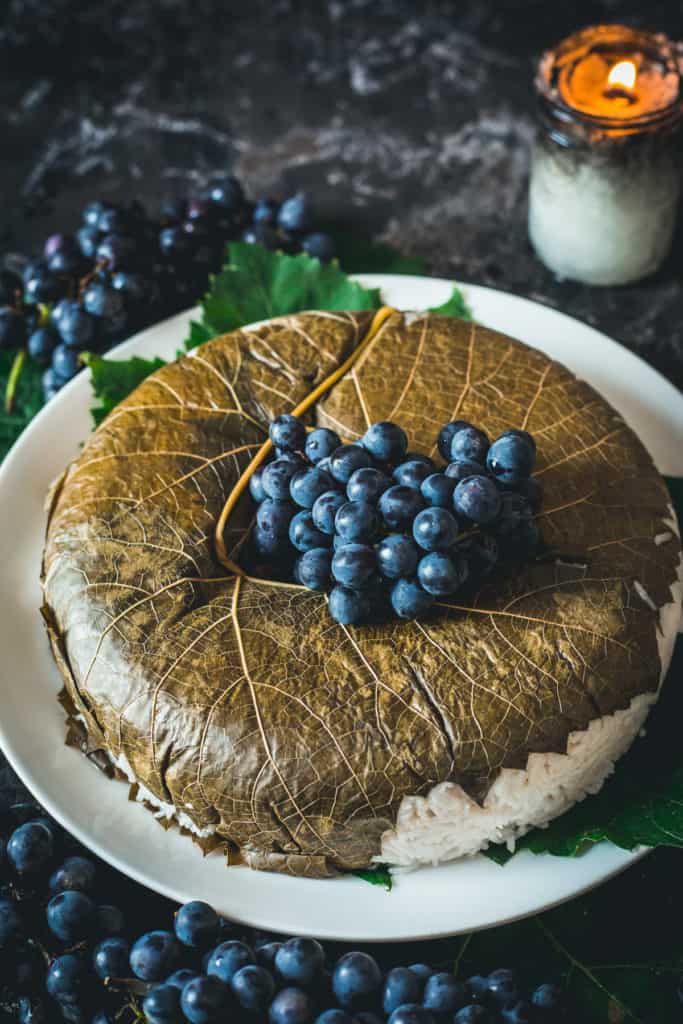 Rice topped with grape leaf and fresh grapes, resting on a large platter and decorated with grapes, candle in background