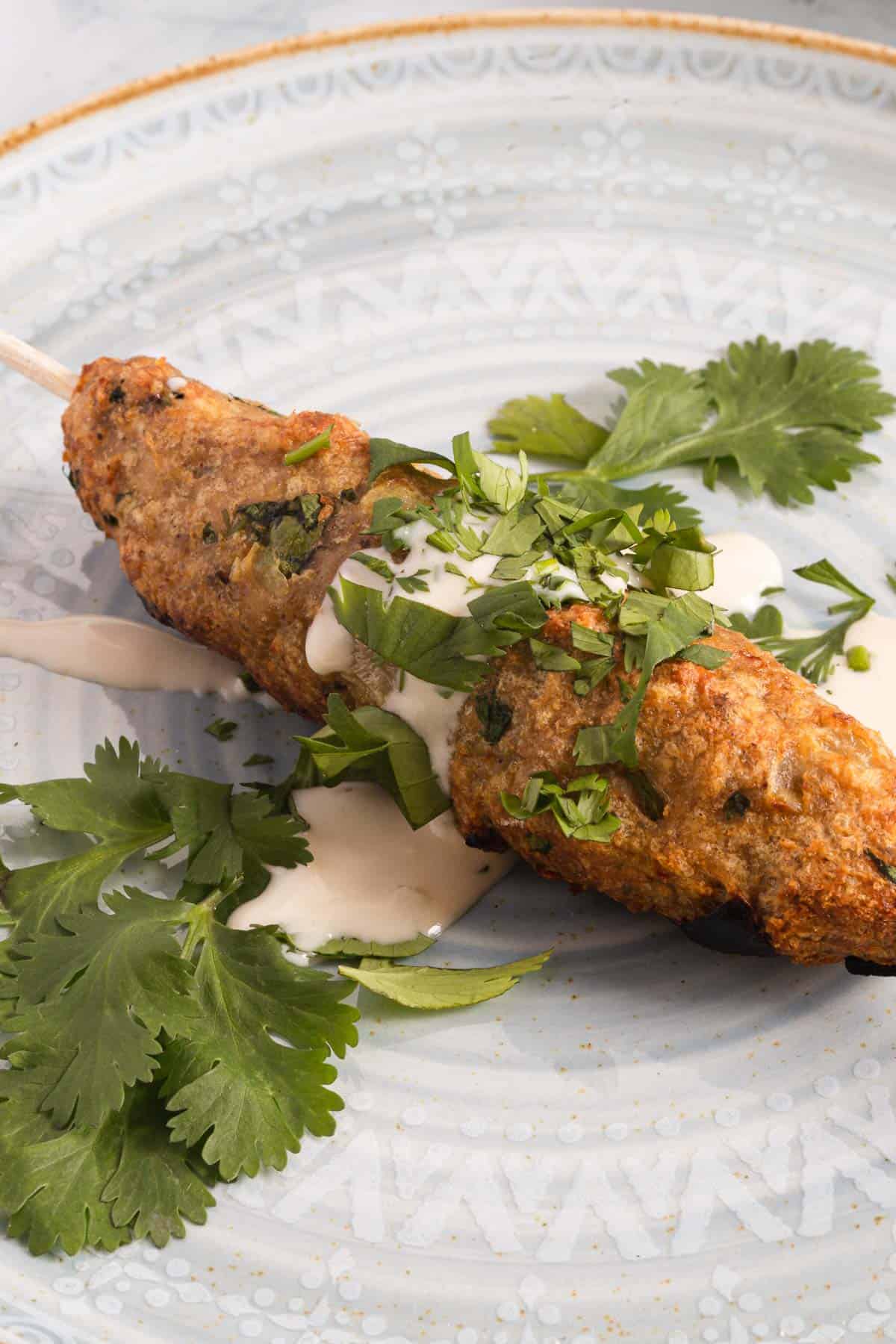 A whole kebab on a skewer on a plate with cilantro.